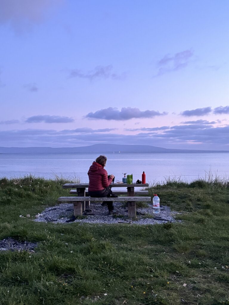Moteris, sėdinti ant suolelio Airijos paplūdimyje, leidžiantis saulei