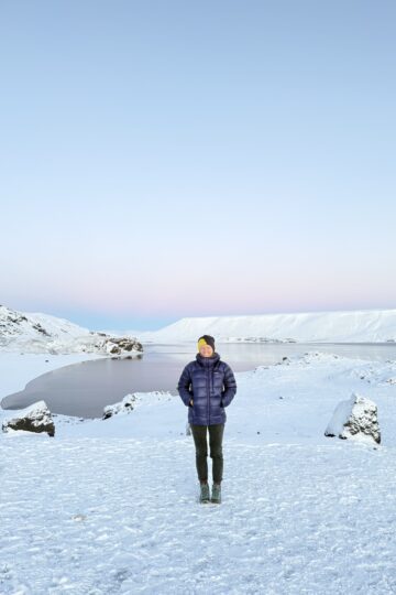 Kleifarvatn ežeras Islandijoje žiemą, šalia jo stovinti moteris ir pastelinis dangus fone