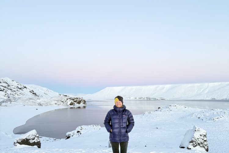 Kleifarvatn ežeras Islandijoje žiemą, šalia jo stovinti moteris ir pastelinis dangus fone